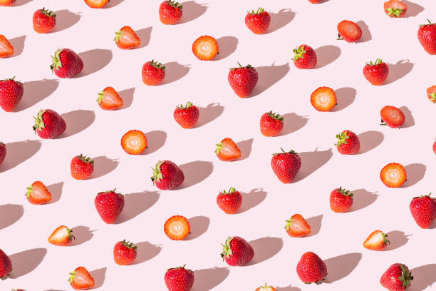 Colorful pattern of strawberries whole and cut on a pink background. View from above.
