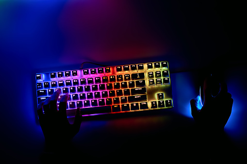 Gamer is playing a computer game, top view. A man is playing a video game, his hands are on the keyboard. Gamer's workspace, mechanical keyboard with RGB color.