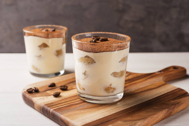 Homemade Italian tiramisu dessert with cocoa powder in glasses on light wooden table. Homemade Italian tiramisu dessert with cocoa powder in glasses on light wooden table. tiramisu glass stock pictures, royalty-free photos & images