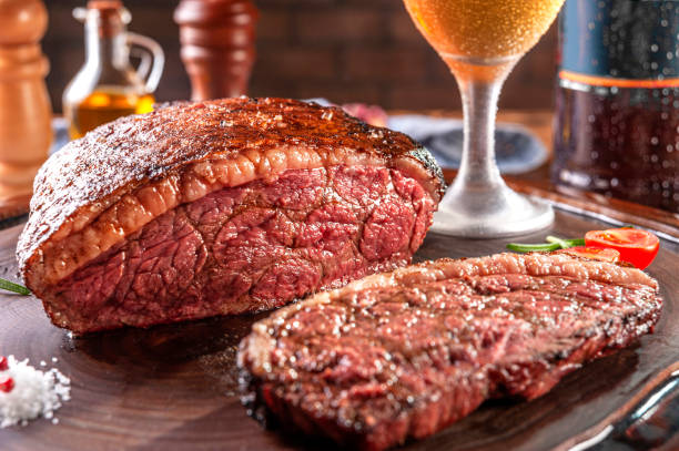 Grilled cap rump steak and beer (brazilian picanha) Grilled sliced cap rump steak with two glasses of beer on wooden cutting board. Marble meat beef (Brazilian picanha). brazilian bbq stock pictures, royalty-free photos & images