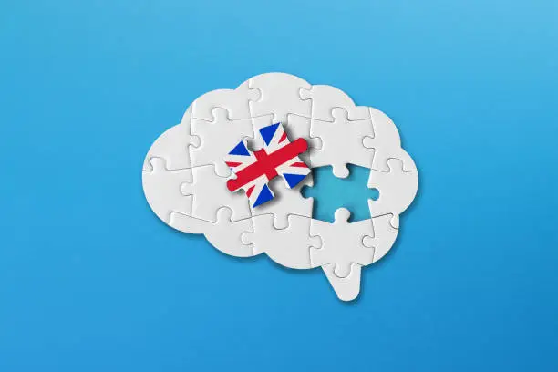 Photo of English learning concept, white jigsaw puzzle pieces with british flag a human brain shape on blue background