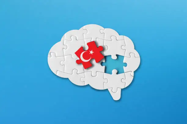 Photo of Turkish learning concept, white jigsaw puzzle pieces with turkish flag a human brain shape on blue background