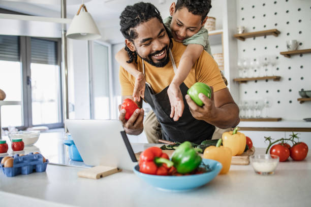 kleiner junge, der spaß mit seinem vater hat, während er eine gesunde mahlzeit zubereitet - child eating healthy eating healthy lifestyle stock-fotos und bilder