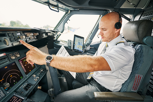 Serious male pilot with a pre-flight checklist in his hand sitting alone in the cockpit