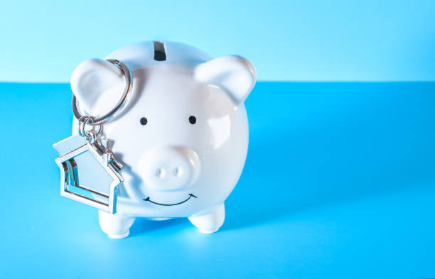 istock White piggy bank and house keychain on blue background. 1336370077