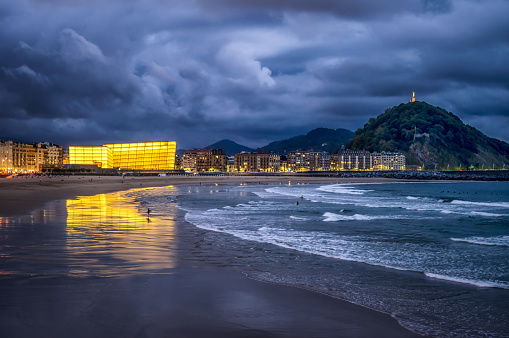 Zurriola beach and mount urgull at dusk with Kursaal Congress Centre reflected on water