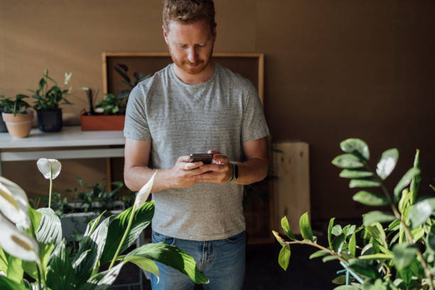 istock Handsome Florist Using Mobile Phone while Working at his Flower Shop 1336373026