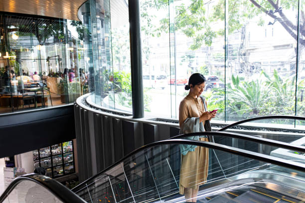 femme asiatique avec un smartphone chevauchant un escalator - escalator photos et images de collection