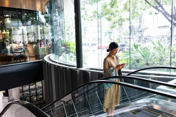 Asian woman using her mobile phone on a shopping mall escalator
