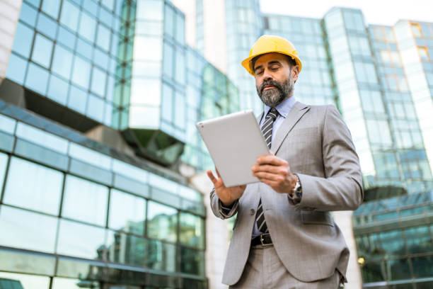 istock Mid adult architect using digital tablet and examining a digital blueprint at financial district. 1336374875
