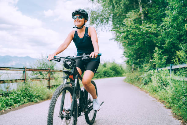 Portrait of a happy smiling woman dressed in cycling clothes, helmet and sunglasses riding a bicycle on the asphalt out-of-town bicycle path. Active sporty people concept image. stock photo