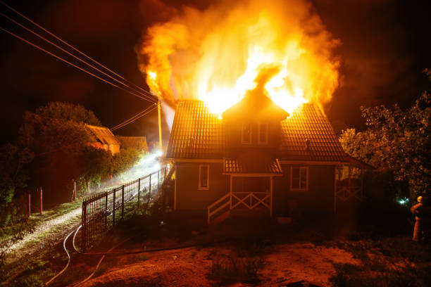 Close-Up Of A Firefighter Spraying Burning House With Hose