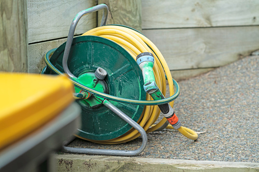 Close up of yellow garden hose beside rubbish bin with yellow lid. The objects are outside at the back of the house beside a retaining wall.