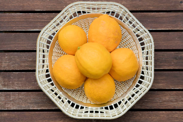 Bowl of six ripe lemons taken from overhead. The bowl is sitting on a slatted wooden table.
