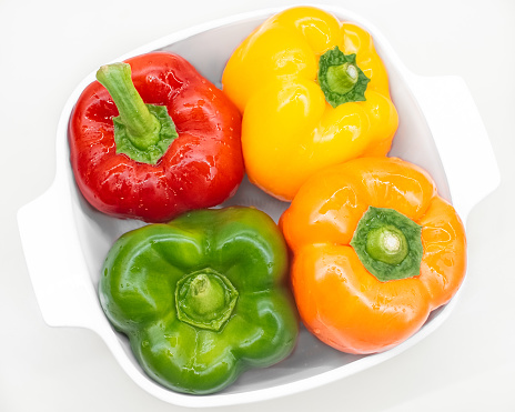 Four Bell Peppers in a variety of colors, in a white dish and viewed from above.