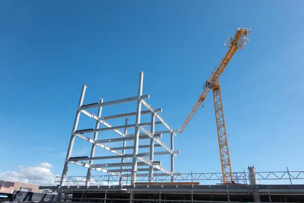 heavy steel frame rising into blue sky as new building being  constructed with high yellow crane.