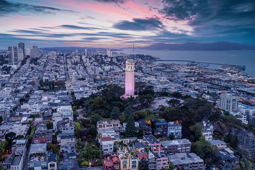 A dramatic sky washed with pinks and lavenders and Coit Tower on Russian Hill illuminated. Golden gate Bridge in the distance.