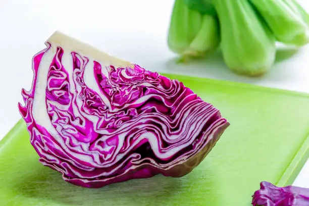 Overhead shot of a quarter purple cabbage on a green cutting board against white background.
