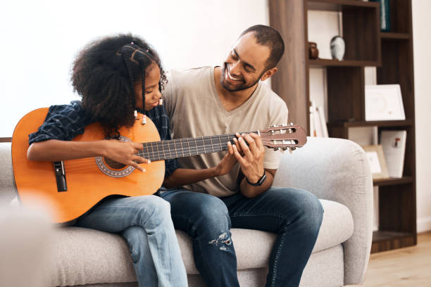 снимок молодой девушки, которая учится играть на гитаре со своим отцом дома - 20s acoustic guitar adult art стоковые фото и изображения