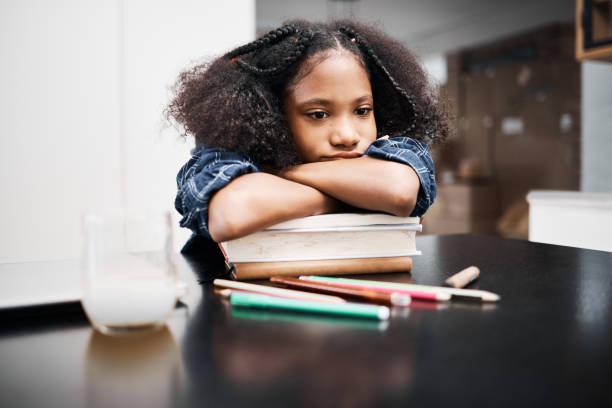 tiro de uma jovem parecendo infeliz enquanto fazia uma tarefa escolar em casa - africa child reading african descent - fotografias e filmes do acervo