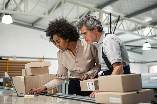 Portrait of warehouse colleagues preparing packages for shipping during daytime