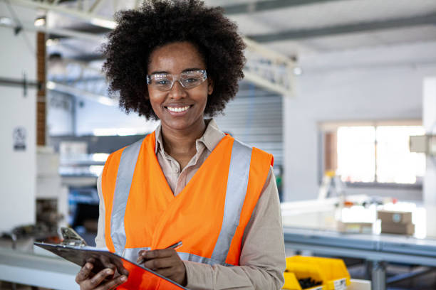 Portrait of smiling female safety engineer holding clipboard while standing inside sustainable factory stock photo