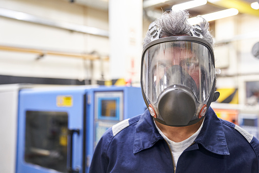 Smiling male industrial technician wearing safety breathing mask inside factory