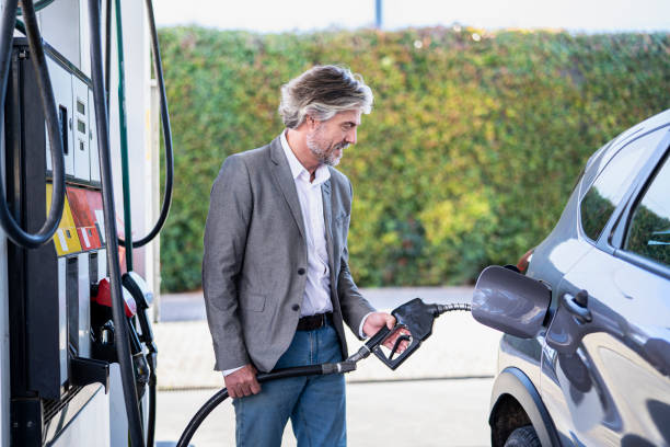 Side view of mature adult man filling fuel tank while standing next to car stock photo