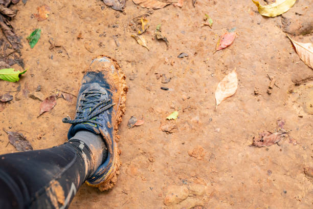 the left foot of a trail runner in running shoes, smeared in orange mud on a rainy day on a dirt road. - mud run imagens e fotografias de stock