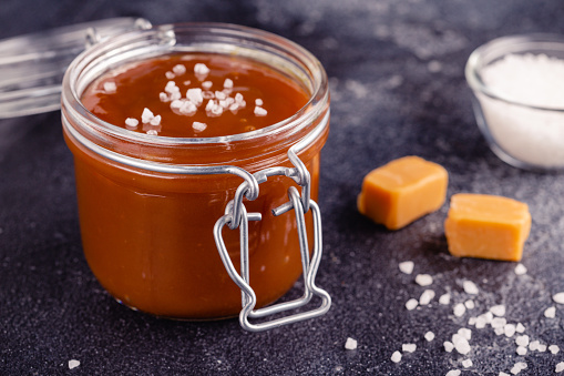 Glass jar with tasty delicious salted caramel, selective focus