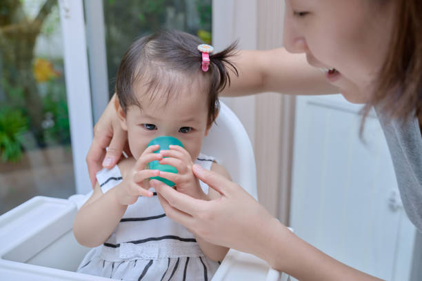 유아는 그녀의 어머니의 도움으로 유리에서 물을 마시고있다 - baby cup 뉴스 사진 이미지