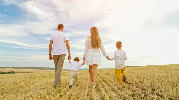 Photo of Family with children walks joining hands on mown wheat field