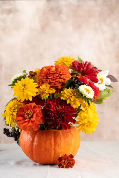 Photo of Bouquet of fresh flowers in pumpkin on table near beige wall