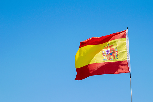 A single Spanish flag blowing in the wind and sunshine against a sky blue background wallpaper