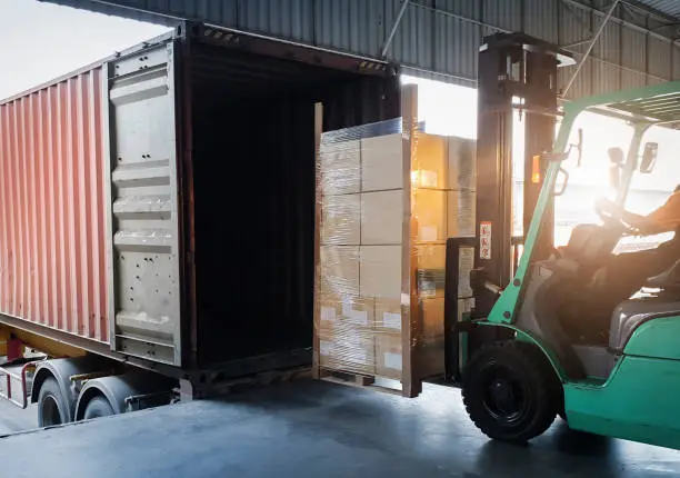 Forklift Tractor Loading Package Boxes into Cargo Container at Dock Warehouse. Delivery Service. Shipping Warehouse Logistics. Cargo Shipment. Freight Truck Transportation.