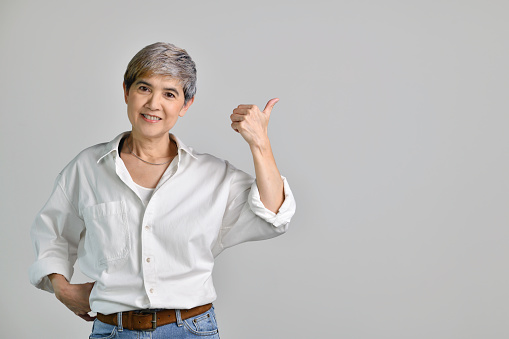 Middle aged Asian woman pointing fingers up at empty copy space for text isolated on white background