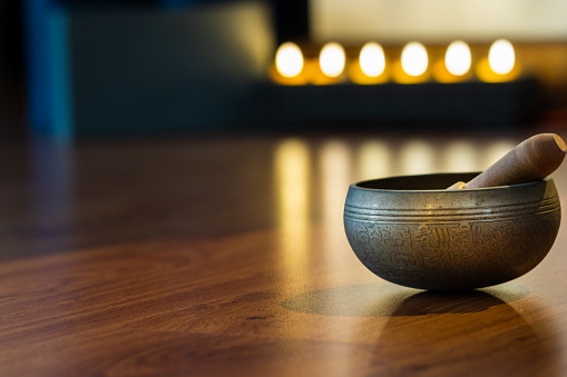 singing bowl on wooden floor on blured candle light background in yoga room