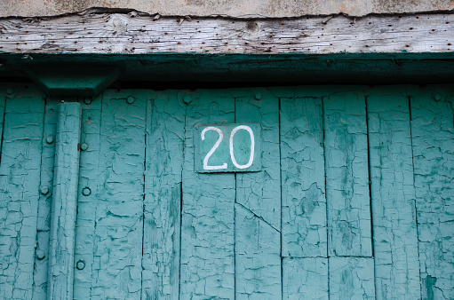 A fence made of wooden boards. House numbering. Old painted boards. Peeling paint.
