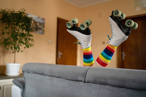 A pair of roller skates and rainbow colored socks on a pair of waving legs in the air, from a sofa in a living room