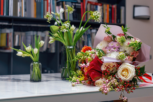 Three beautiful spring bouquets. Flowers arrangements with various of colors in glass vase on white table. Blurred background with bookshelves