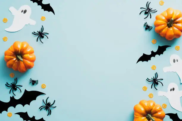 Photo of Halloween flat lay composition with orange pumpkins, ghosts, spiders, bats on blue background. Happy Halloween holiday greeting card mockup. Flat lay, top view, copy space.