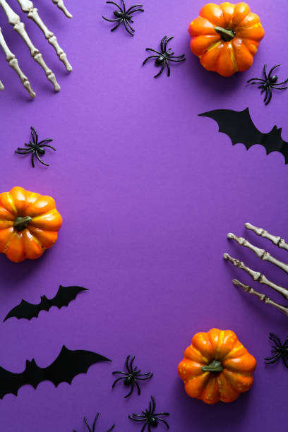 Halloween poster with festive decorations, pumpkins, spiders, skeletons hands, bats on purple background. Flat lay, top view, overhead. Halloween poster with festive decorations, pumpkins, spiders, skeletons hands, bats on purple background. Flat lay, top view, overhead. bat animal photos stock pictures, royalty-free photos & images