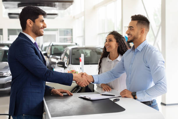 Smiling middle-eastern man and woman buying car at salon Smiling middle-eastern young man and woman buying car at auto salon, handsome arab guy shaking sales assistant hand, making successful deal, happy family got brand new luxury car, side view car dealership stock pictures, royalty-free photos & images
