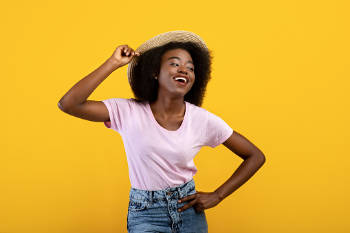 Portrait of pretty african american lady in casual clothes and straw hat on yelow studio background
