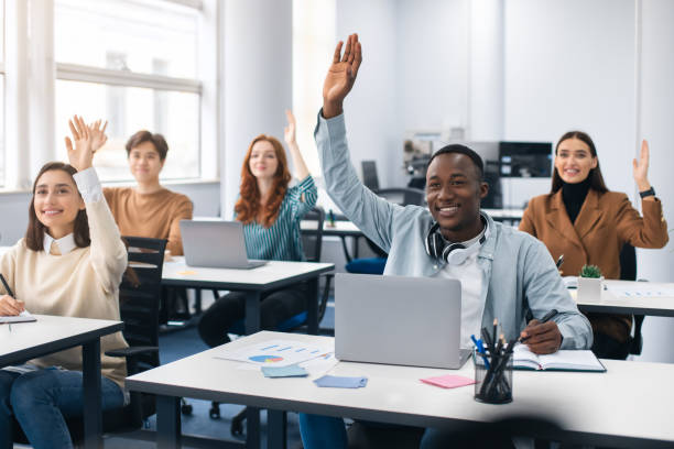 Portrait of diverse students raising hands at modern classroom Training Class And Knowledge Concept. Diverse Group Of Smiling Multicultural People Raising Hands Up Asking Coach a Question Or Answering, Sitting With Laptops At Desks In Modern Classroom professor business classroom computer stock pictures, royalty-free photos & images