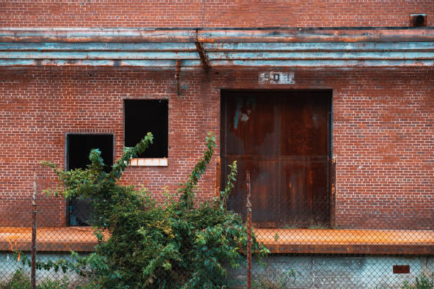 istock Rusted factory doors set in brick wall on abandoned loading dock with chainlink fence in foreground 1336472724
