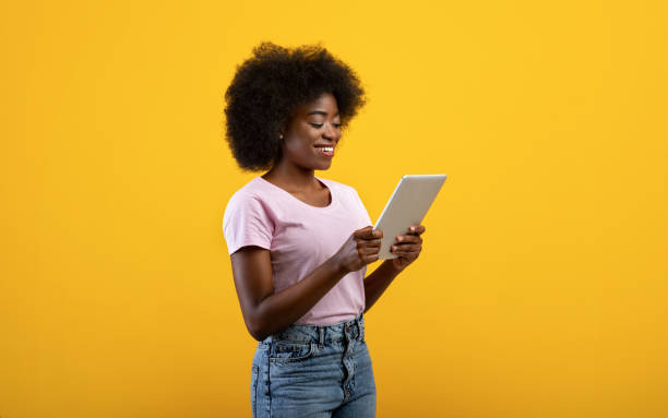 istock Young black lady with modern digital tablet, using mobile application on pad, posing on yellow studio background 1336474815