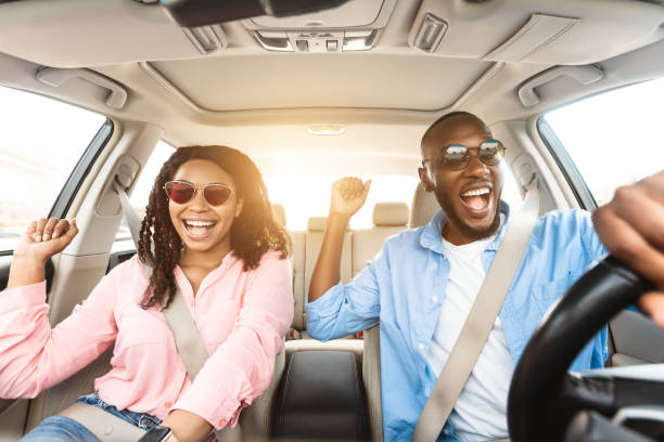 Happy black couple in sunglasses enjoying music driving luxury car Summer Holidays And Roadtrip Concept. Front view portrait of excited black couple in sunglasses driving car, dancing to music and singing favorite song, going on vacation for rest and relax, sun flare car interior stock pictures, royalty-free photos & images
