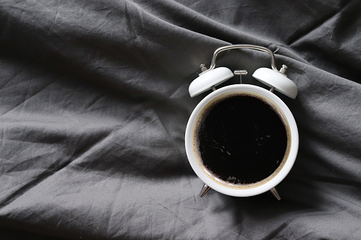 Coffee in the alarm clock on a gray background. Espresso in a mug in the shape of a clock. The concept of morning awakening. An invigorating drink.