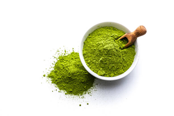 Matcha tea powder shot from above on white background Overhead view of Matcha tea powder in a white bowl isolated on white background. Some Matcha powder is spilled on the background. A wooden serving scoop complete the composition. High resolution 42Mp studio digital capture taken with Sony A7rII and Sony FE 90mm f2.8 macro G OSS lens green tea powder stock pictures, royalty-free photos & images